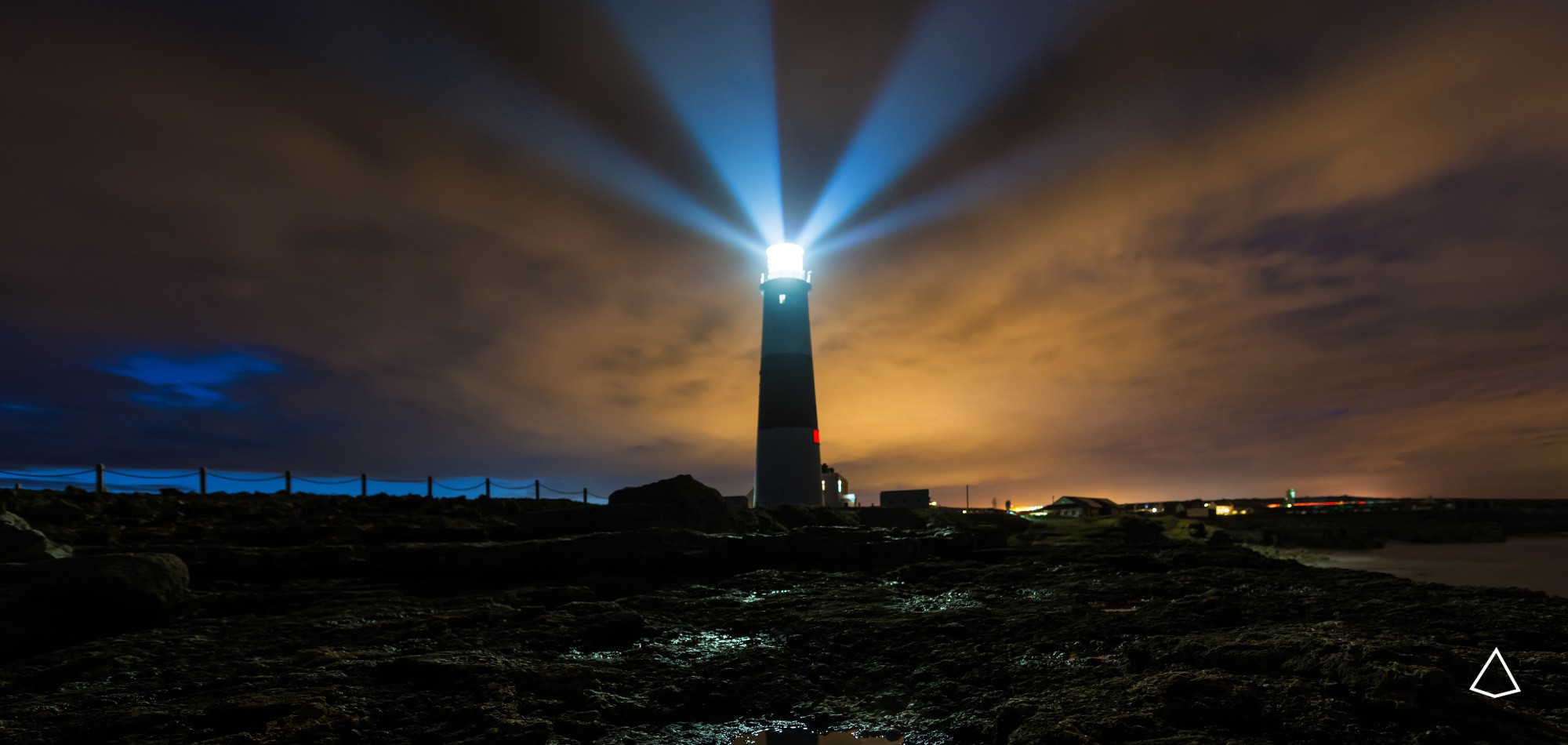 Foto in notturna dal basso di un faro che illumina le rocce.