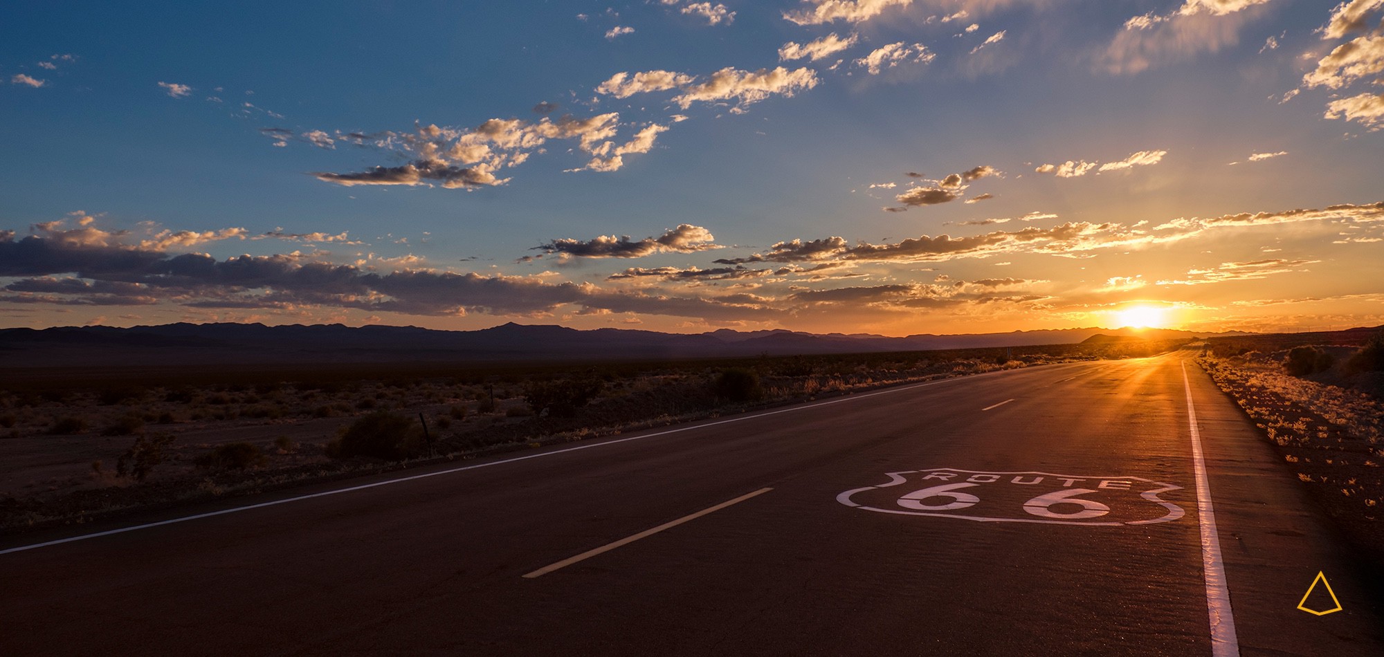 Route 66 al tramonto con il sole che illumina la strada ed un cielo poco nuvoloso.