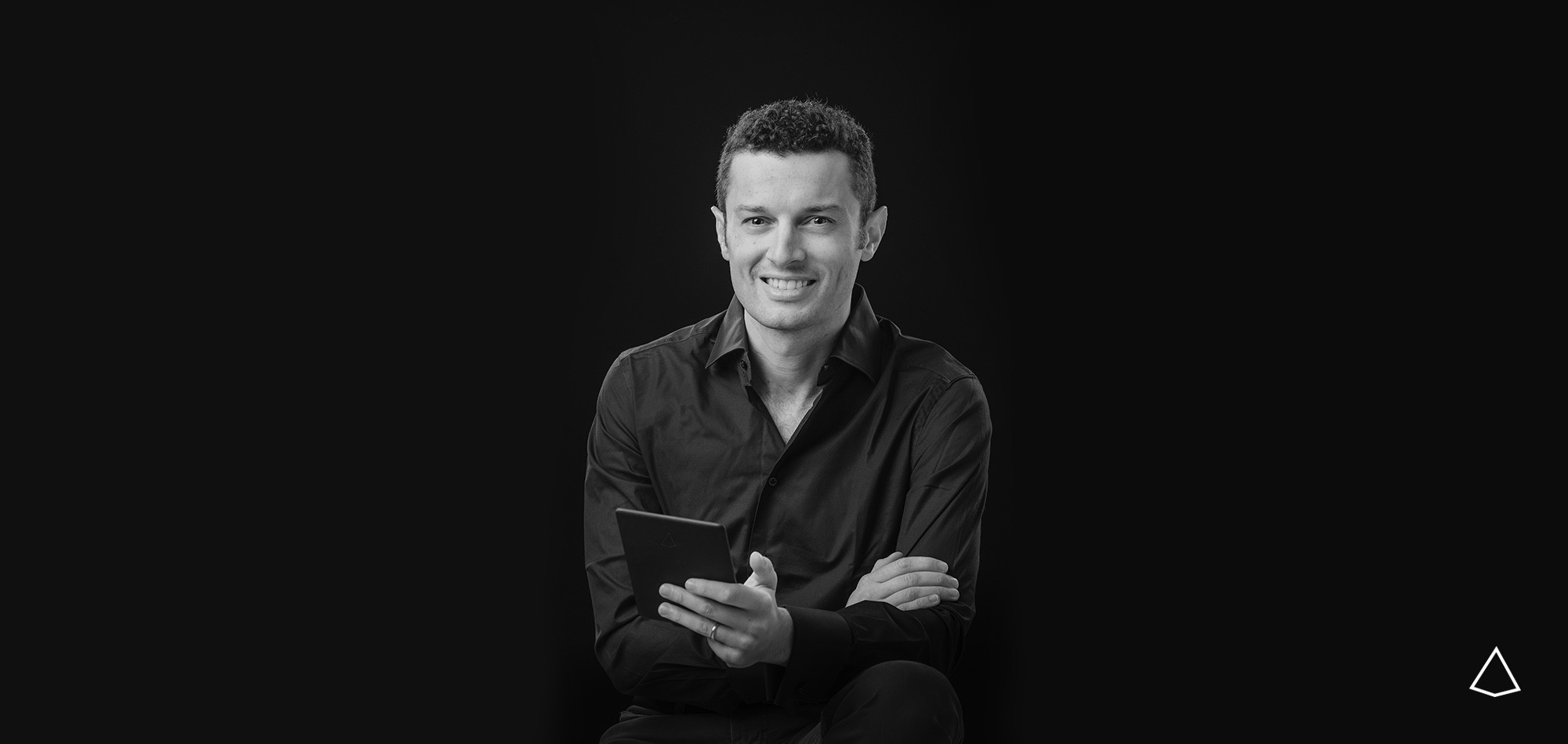 Liborio Fedele sorridente con tablet in mano che guarda in camera in bianco e nero su sfondo isolato.