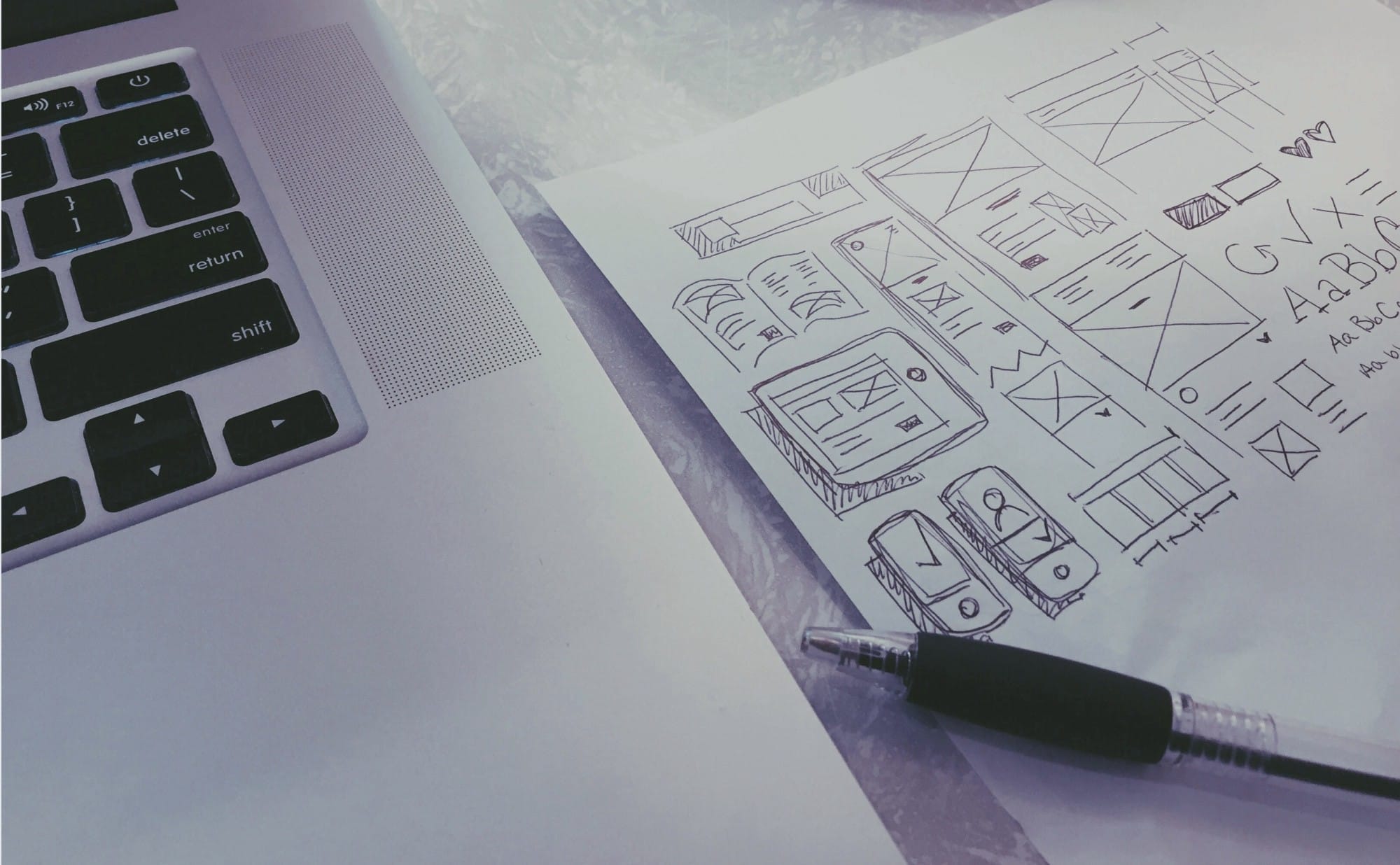 Wireframe di pagine web accanto a un laptop durante la progettazione della struttura di un sito.